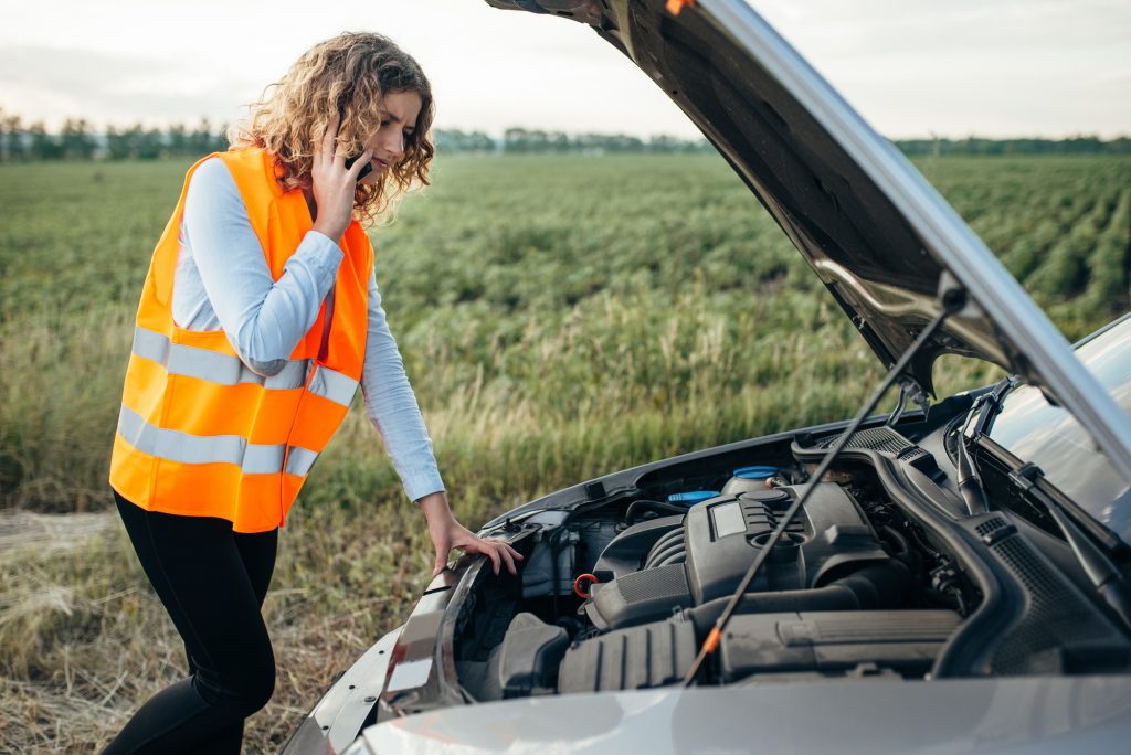 Girl in reflecting vest with phone, broken car