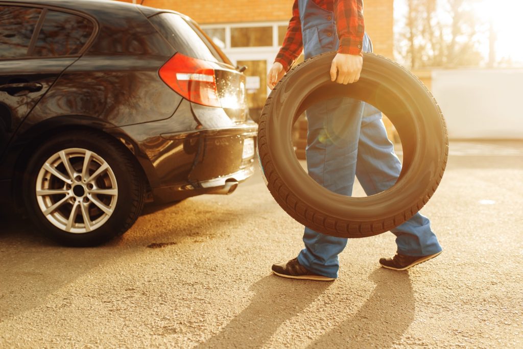 Male worker in uniform holds tyre, tire service